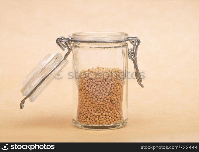 Mustard seeds in glass on brown background