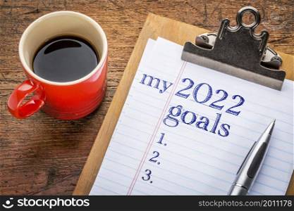 my 2022 goals list on clipboard and coffee against grunge wood desk, setting New Year goals and resolutions