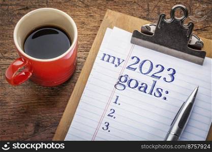 my 2023 goals list on clipboard and coffee against grunge wood desk, setting New Year goals and resolutions