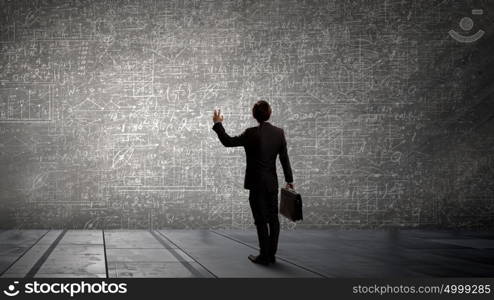 My business strategy. Rear view of businessman looking at chalk business sketches on wall
