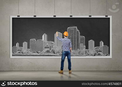 My development project. Rear view of man engineer in helmet drawing on chalkboard