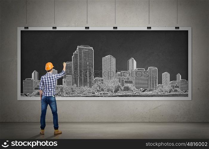My development project. Rear view of man engineer in helmet drawing on chalkboard