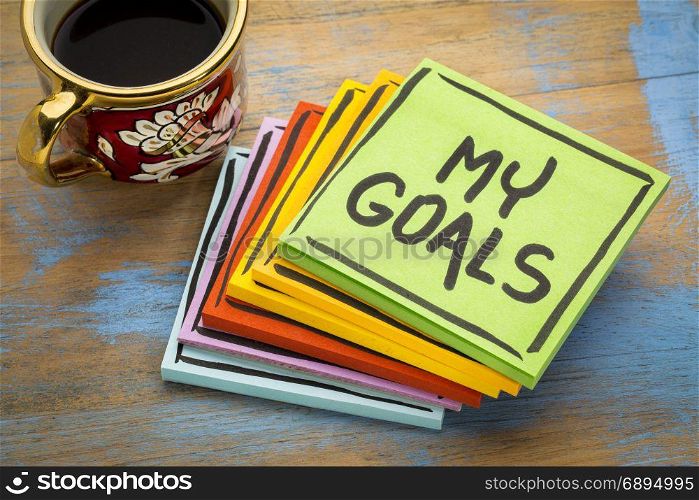 My goals - handwriting in black ink on a sticky note with a cup of espresso coffee