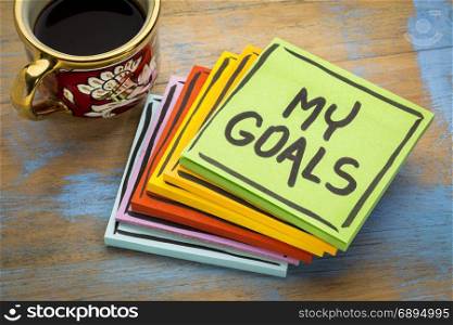 My goals - handwriting in black ink on a sticky note with a cup of espresso coffee