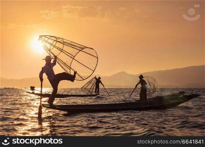 Myanmar travel attraction landmark - three traditional Burmese fishermen at Inle lake, Myanmar famous for their distinctive one legged rowing style. With lens flare.  Traditional Burmese fisherman at Inle lake, Myanmar