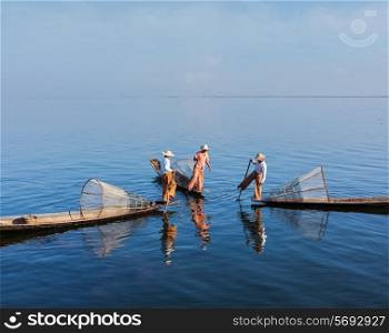 Myanmar travel attraction landmark - three traditional Burmese fishermen with fishing nets on boats at Inle lake in Myanmar famous for their distinctive one legged rowing style