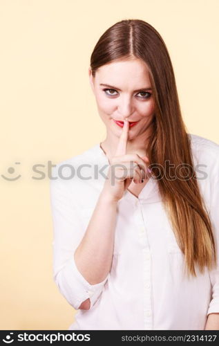 Mysterious, enigmatic brunette woman showing silence gesture with finger close to mouth.. Mysterious woman showing silence gesture with finger