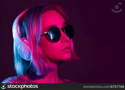 Mysterious hipster teenager in sunglasses listening to music with headphones. Portrait of millennial pretty girl with short hairstyle with neon light. Dyed blue and pink hair. Mysterious hipster teenager in sunglasses listening to music with headphones. Portrait of millennial pretty girl with short hairstyle with neon light. Dyed blue and pink hair.