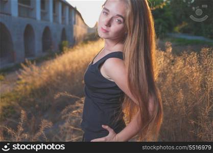 mysterious looking image of 20s young female with long blond hair posing against sunset golden light in park. Backlit shot.