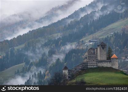 Mystic cloudy and foggy autumn alpine mountain slopes scene. Austrian Lienzer Dolomiten Alps and Heinfels castle, Sillian, Austria.