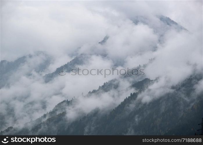 Mystic cloudy and foggy autumn alpine mountain slopes scene. Austrian Lienzer Dolomiten Alps. Peaceful picturesque traveling, seasonal, nature and countryside beauty concept scene.