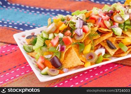 Nachos and vegetables on plate on colorful towels.