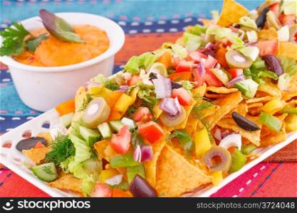 Nachos, vegetables and cheese sauce on colorful towels.