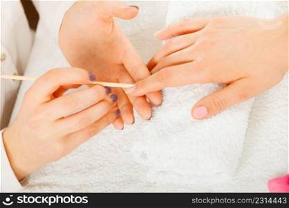 Nail care, beauty wellness spa treatment concept. Woman beautician preparing nails before manicure, pushing back cuticles using wooden stick. Beautician preparing nails before manicure, pushing back cuticles