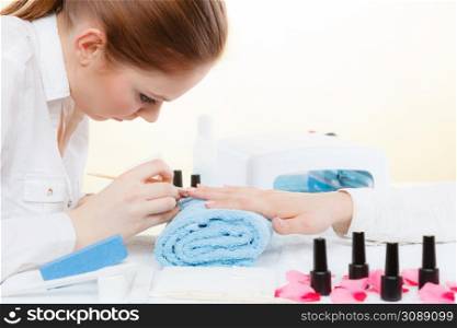 Nail care, beauty wellness spa treatment concept. Woman beautician preparing nails before manicure, pushing back cuticles using wooden stick. Beautician preparing nails before manicure, pushing back cuticles