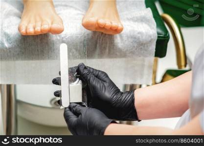 Nail file tool in hands of chiropodist before procedure files nails on toes in a nail salon. Nail file tool in hands