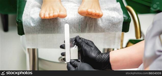 Nail file tool in hands of chiropodist before procedure files nails on toes in a nail salon. Nail file tool in hands