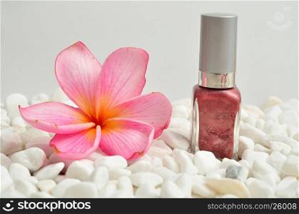Nail polish displayed on white pebbles with a pink frangipani flower