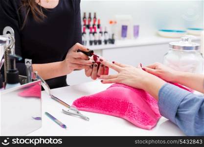 Nail saloon woman painting color nail polish in hands over pillow with pink towel