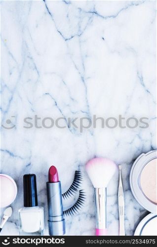 nail varnish blushes lipstick tweezers compact powder eyelashes arranged marble textured background