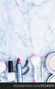 nail varnish blushes lipstick tweezers compact powder eyelashes arranged marble textured background