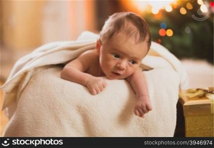 Naked baby boy lying on stomach in basket next to fireplace
