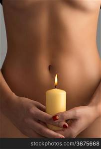 naked belly is behind one yellow candel taked with two hands and fire is near navel