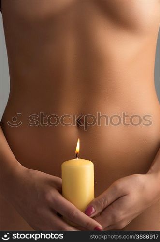 naked belly is behind one yellow candel taked with two hands with red nails