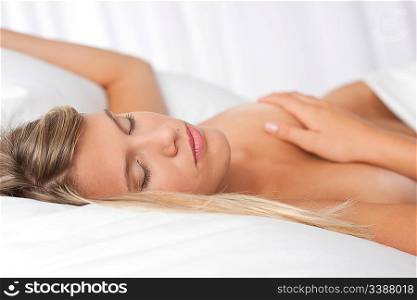 Naked blond woman lying in white bed and sleeping