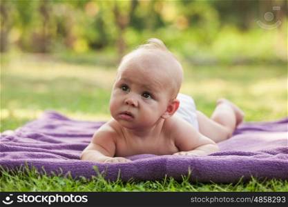 Naked little boy wearing a diaper learning to crawl on green grass. Little boy crawling on lawn