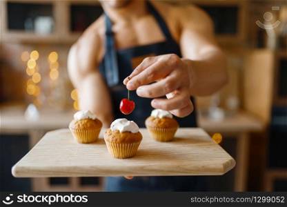 Naked man in apron cooking dessert with cherry on the kitchen. Nude male person preparing breakfast at home, food preparation. Naked man in apron cooking dessert on the kitchen