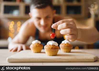 Naked man in apron cooking dessert with cherry on the kitchen. Nude male person preparing breakfast at home, food preparation without clothes