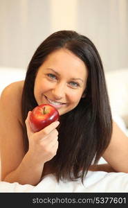 Naked woman eating an apple in bed