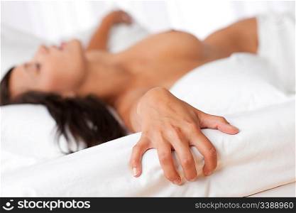 Naked woman lying in bed, focus on hand, shallow DOF