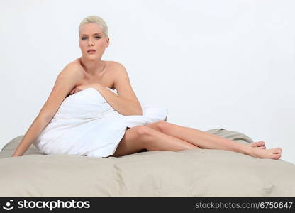 Naked woman sitting on a bed behind a pillow