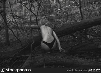 Naked woman sitting on fallen tree monochrome scenic photography. Picture of person with deep forest on background. High quality wallpaper. Photo concept for ads, travel blog, magazine, article. Naked woman sitting on fallen tree monochrome scenic photography