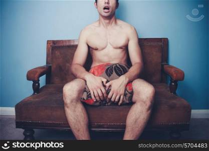 Naked young man is sitting on a sofa