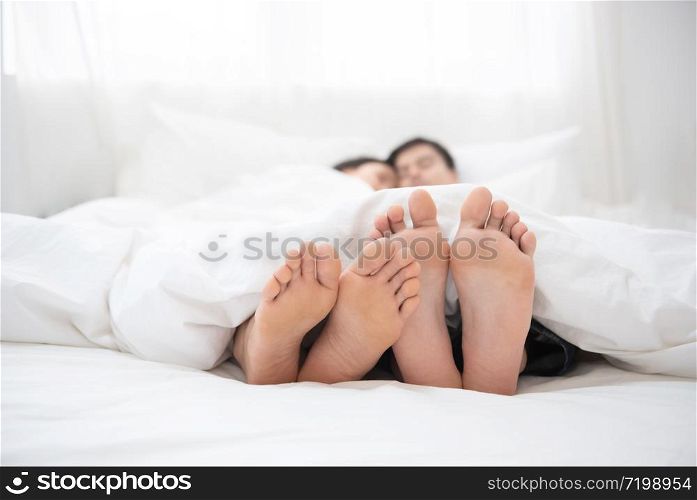 Napping man woman barefoot lying under covers bed hotel room, closer up on couple feet.