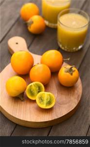 Naranjilla or Lulo fruits (lat. Solanum quitoense) on wooden board with freshly prepared naranjilla juice in the back (Selective Focus, Focus on the first naranjilla half)