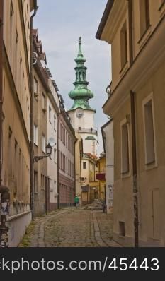 Narrow crooked cobbled bystreet with church tower in Bratislava. Narrow Crooked bystreet in Bratislava