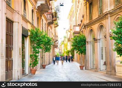Narrow street with walking people and trees in ceramic pots in Milan, Italy