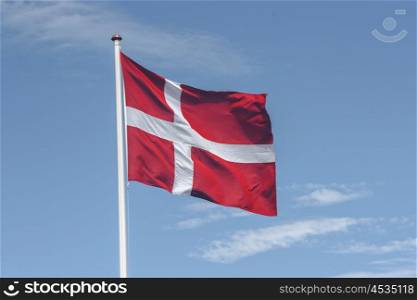 National flag of Denmark in red and white on blue sky