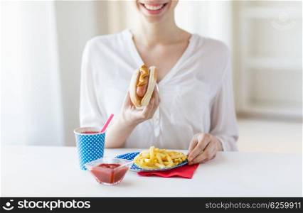 national holidays, celebration, food and patriotism concept - close up of happy woman eating hot dog and french fries with drink in paper cup at 4th july at party on american independence day