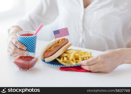 national holidays, celebration, food and patriotism concept - close up of woman eating hot dog and french fries with drink in disposable paper cup at 4th july at party on american independence day