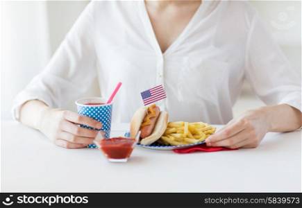 national holidays, celebration, food and patriotism concept - close up of woman eating hot dog and french fries with drink in disposable paper cup at 4th july at party on american independence day