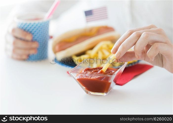 national holidays, celebration, food and patriotism concept - close up of woman eating french fries with hot dog and drinking juice from paper cup at 4th july at party on american independence day