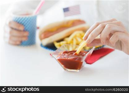 national holidays, celebration, food and patriotism concept - close up of woman eating french fries with hot dog and drinking juice from paper cup at 4th july at party on american independence day