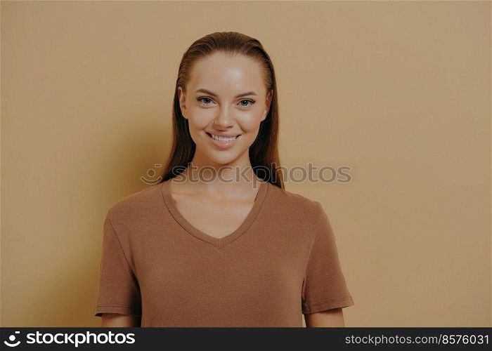 Natural beauty. Young charming woman with healthy skin and hair smiling at camera, attractive female with daily makeup wearing basic beige t-shirt, demonstrating positive emotions and happiness. Natural beauty. Young charming woman with daily makeup wearing basic beige t-shirt smiling at camera