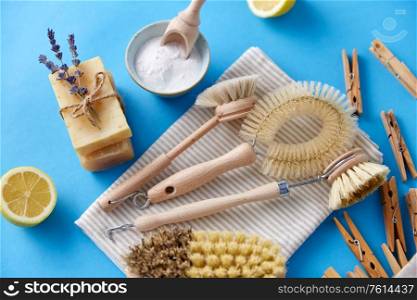 natural cleaning stuff, sustainability and eco living concept - different brushes, lemon, wooden clothespins and washing soda with soap on blue background. cleaning brushes, lemon and wooden clothespins