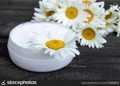 natural cosmetic cream near chamomile flowers on a wooden table. cosmetic cream near chamomile flowers on a wooden table